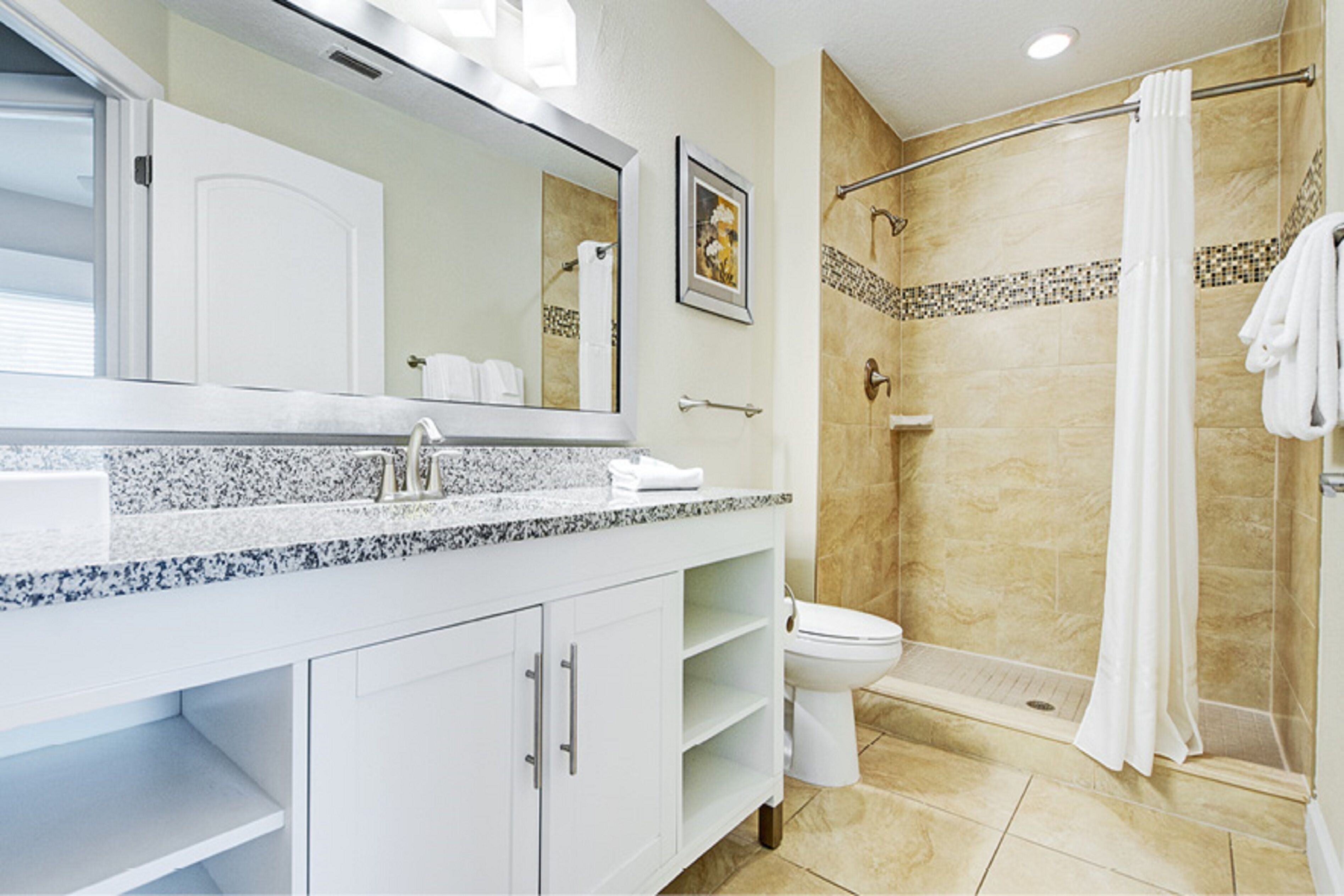 A modern bathroom with a granite countertop, a white sink, a toilet, and a shower area.