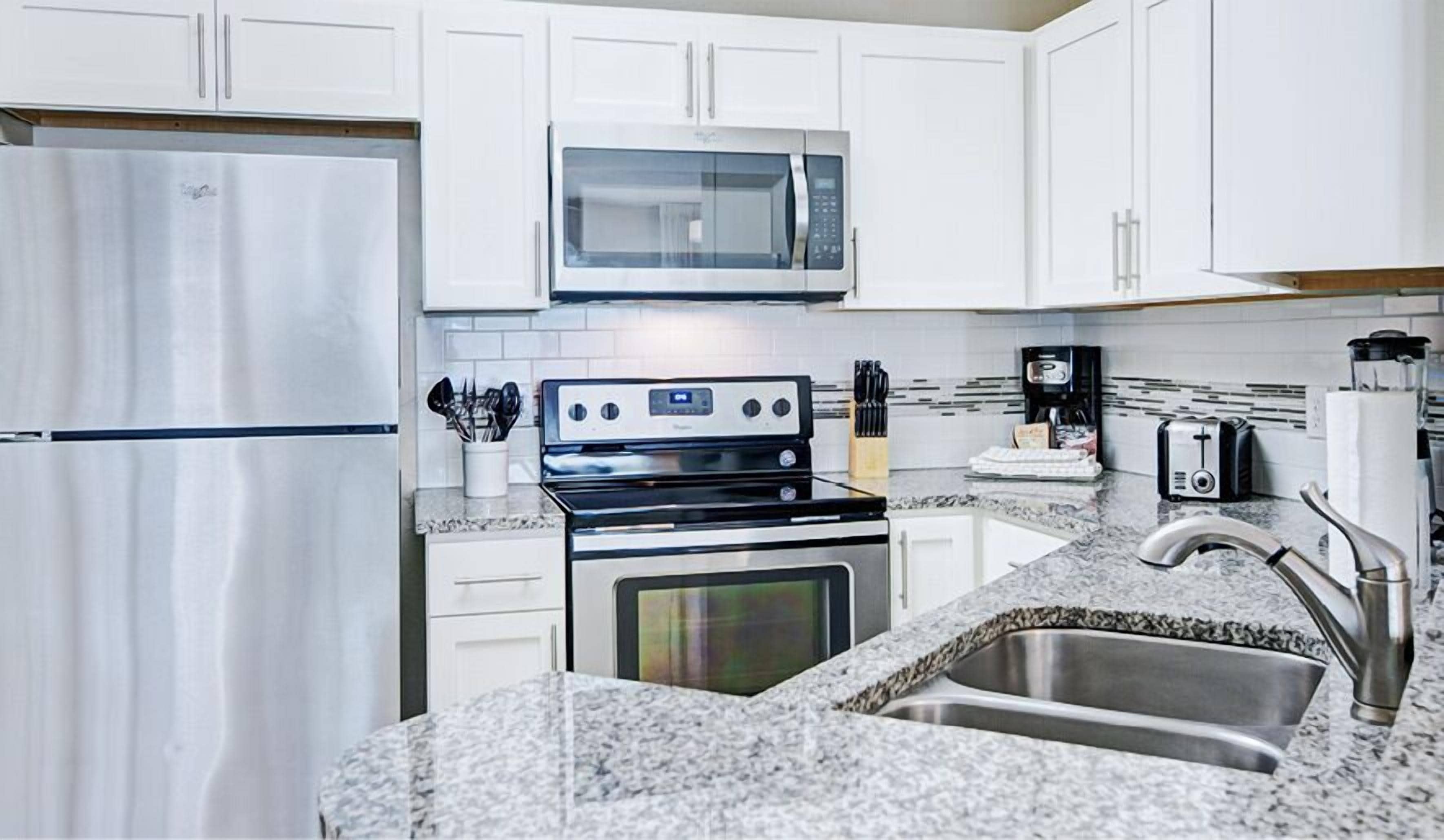 A modern kitchen with white cabinets, a stainless steel refrigerator, a microwave, a stove, and a sink.