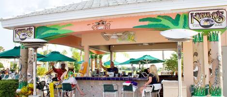Un bar de style tiki avec des places assises en plein air, un comptoir et une fresque murale colorée.