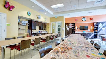 A dining area with a long table covered in a colorful tablecloth, surrounded by chairs.