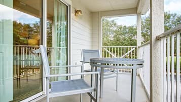 A balcony with a table and two chairs, a glass door, and a white railing.