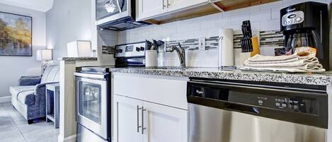 A modern kitchen with stainless steel appliances, white cabinetry, and a granite countertop.