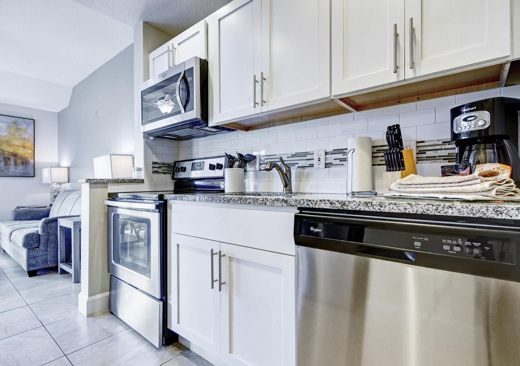 A modern kitchen with stainless steel appliances, white cabinetry, and a granite countertop.