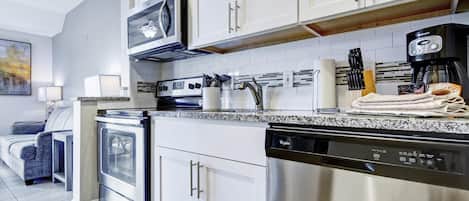 A modern kitchen with stainless steel appliances, white cabinetry, and a granite countertop.