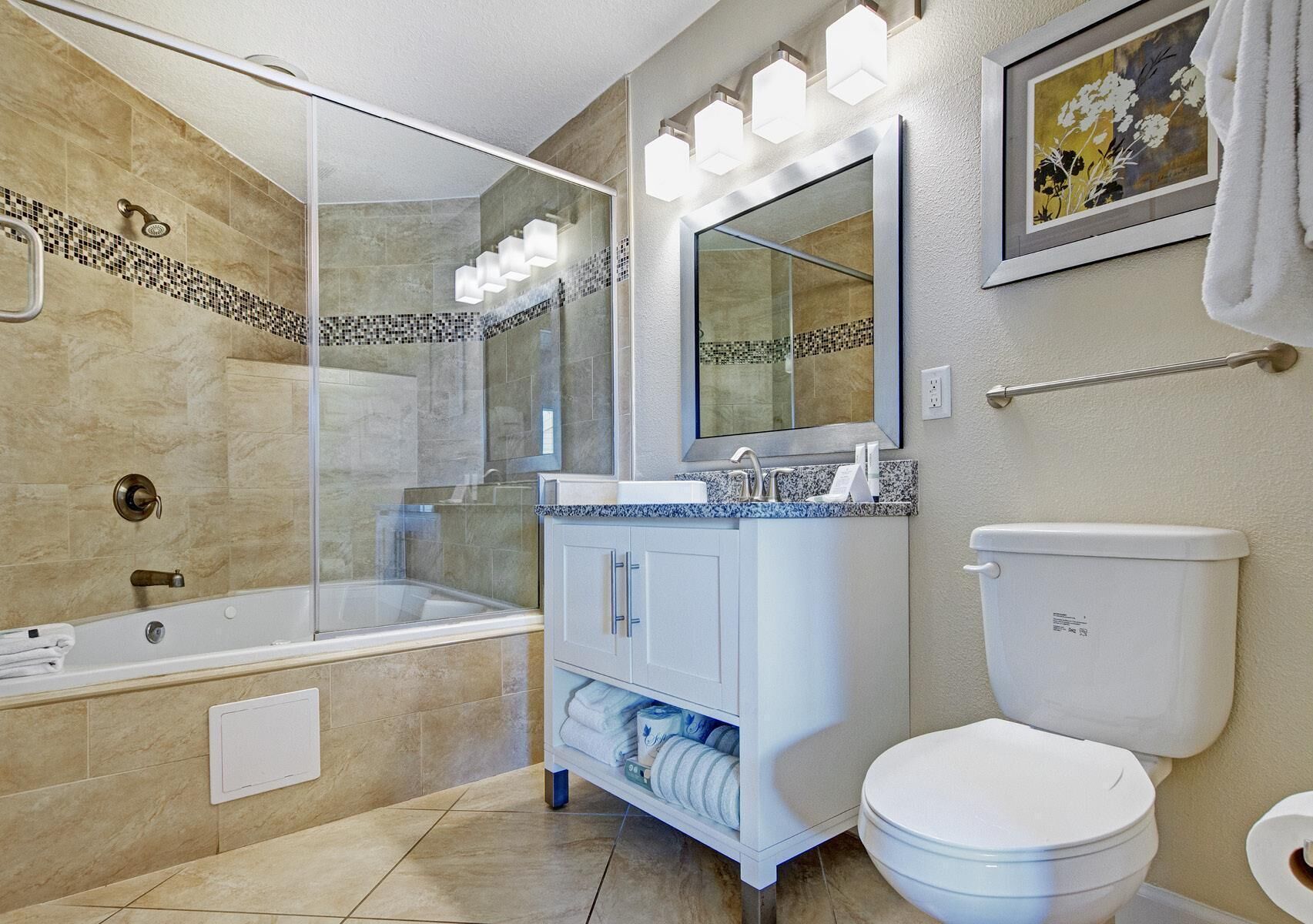 A modern bathroom with a glass-enclosed shower, a freestanding bathtub, a vanity with a sink and mirror, and a toilet.