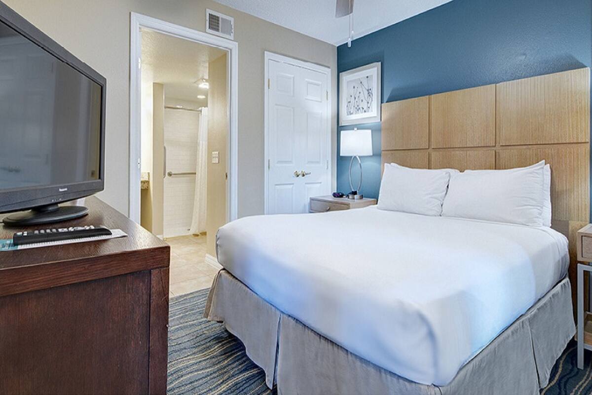 Una habitación de hotel con cama, televisión, escritorio y puerta que da a un baño.