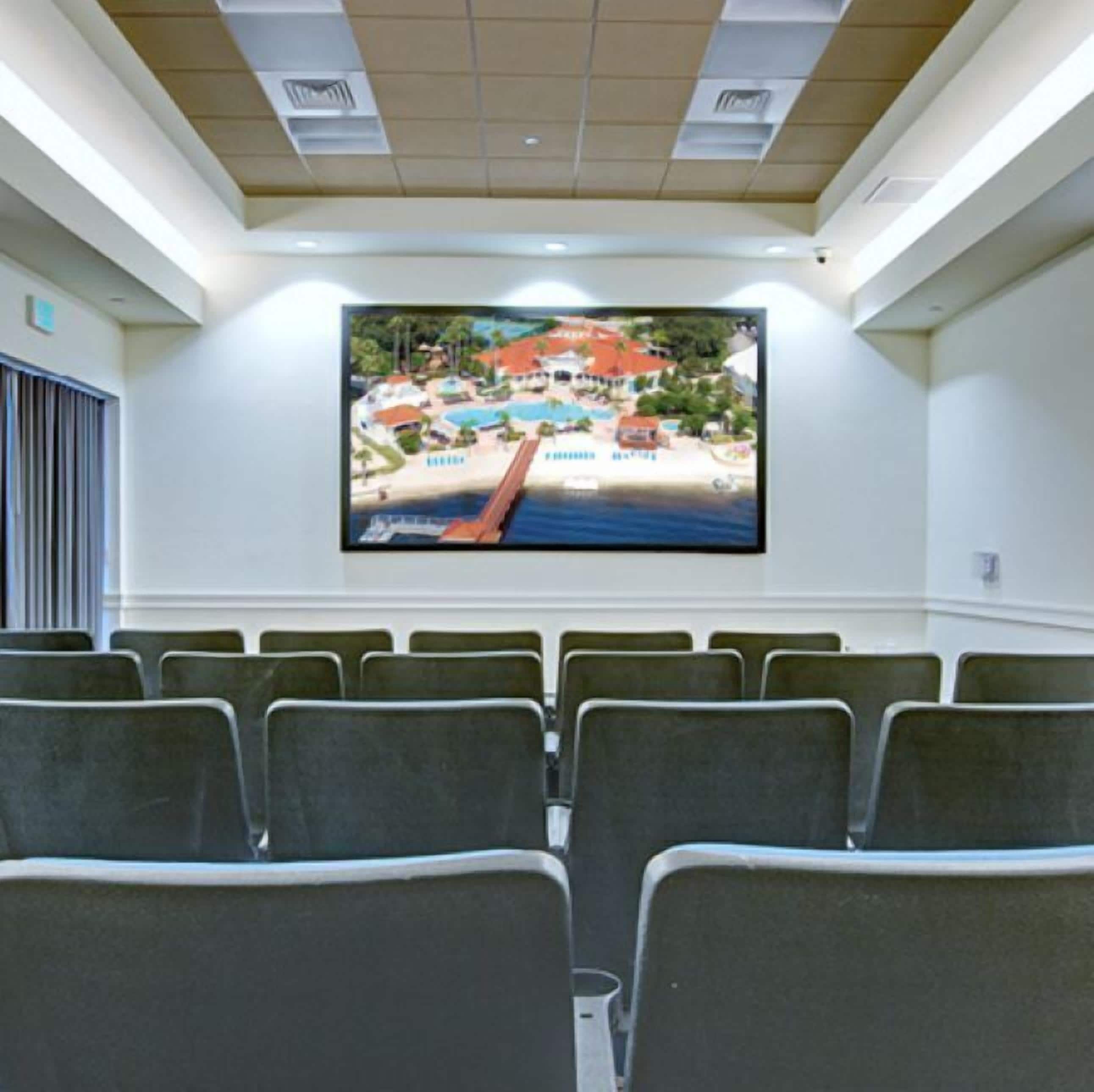 Une salle de conférence dotée d’un grand écran affichant une image d’un complexe hôtelier, de rangées de chaises et d’un plafond équipé d’un éclairage encastré.