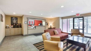 A hotel lobby with a reception desk, a coffee station, a red sofa, a beige armchair, and a striped rug. - Extended Stay America Suites Cleveland Westlake (Westlake)