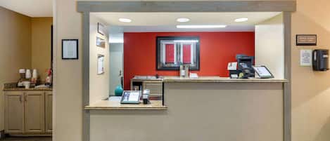 A reception area with a counter, a red wall, framed pictures, a window, and a sign indicating office hours.