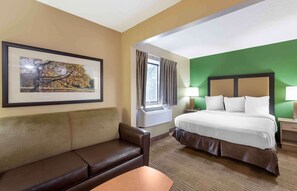 A hotel room with a bed, a couch, a window with curtains, an air conditioning unit, and a framed picture on the wall. - Extended Stay America Suites Cleveland Westlake (Westlake)