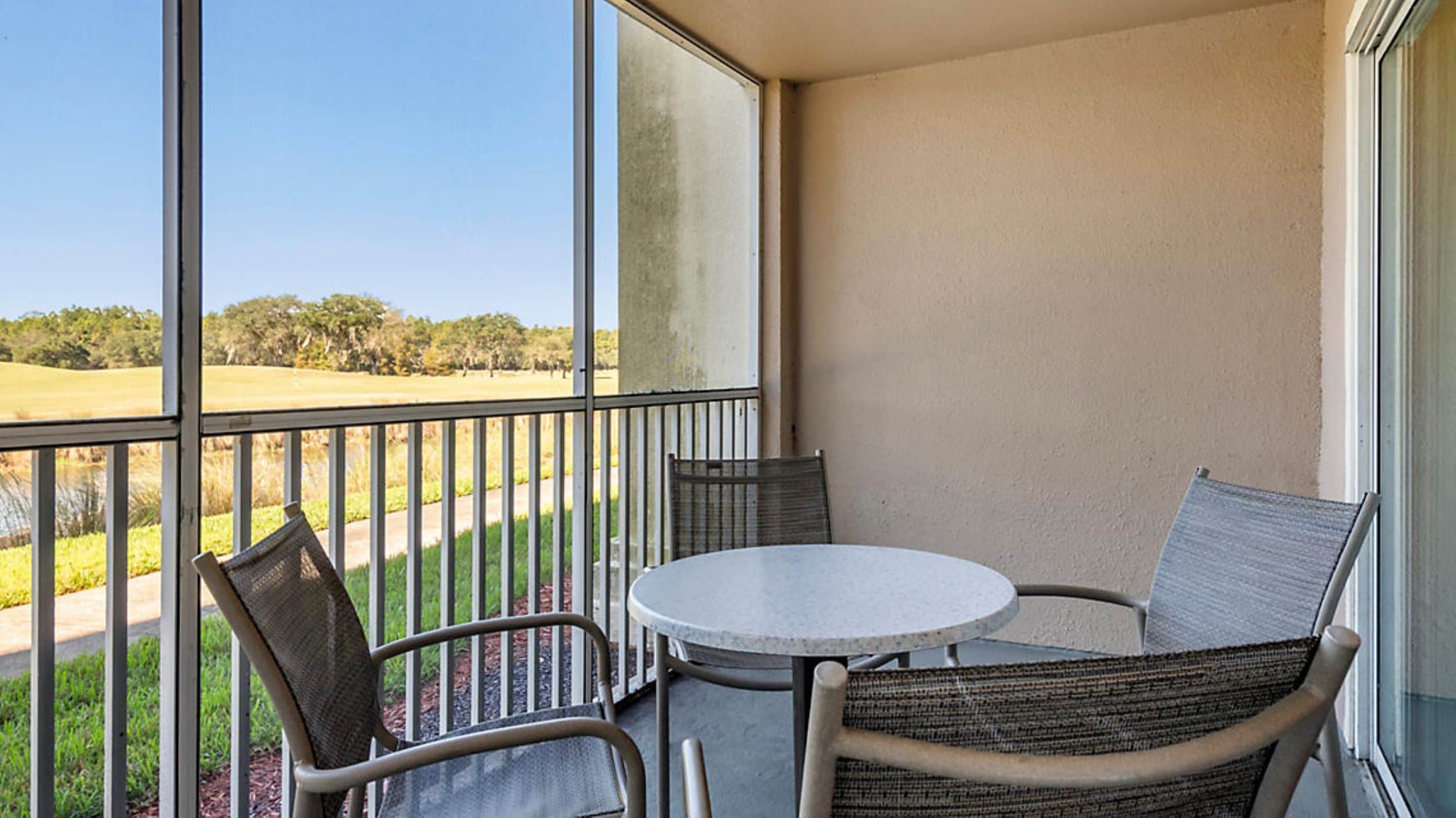 A balcony with a round table and two wicker chairs, overlooking a golf course.