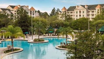 A resort with a large central pool surrounded by lounge chairs and palm trees.
