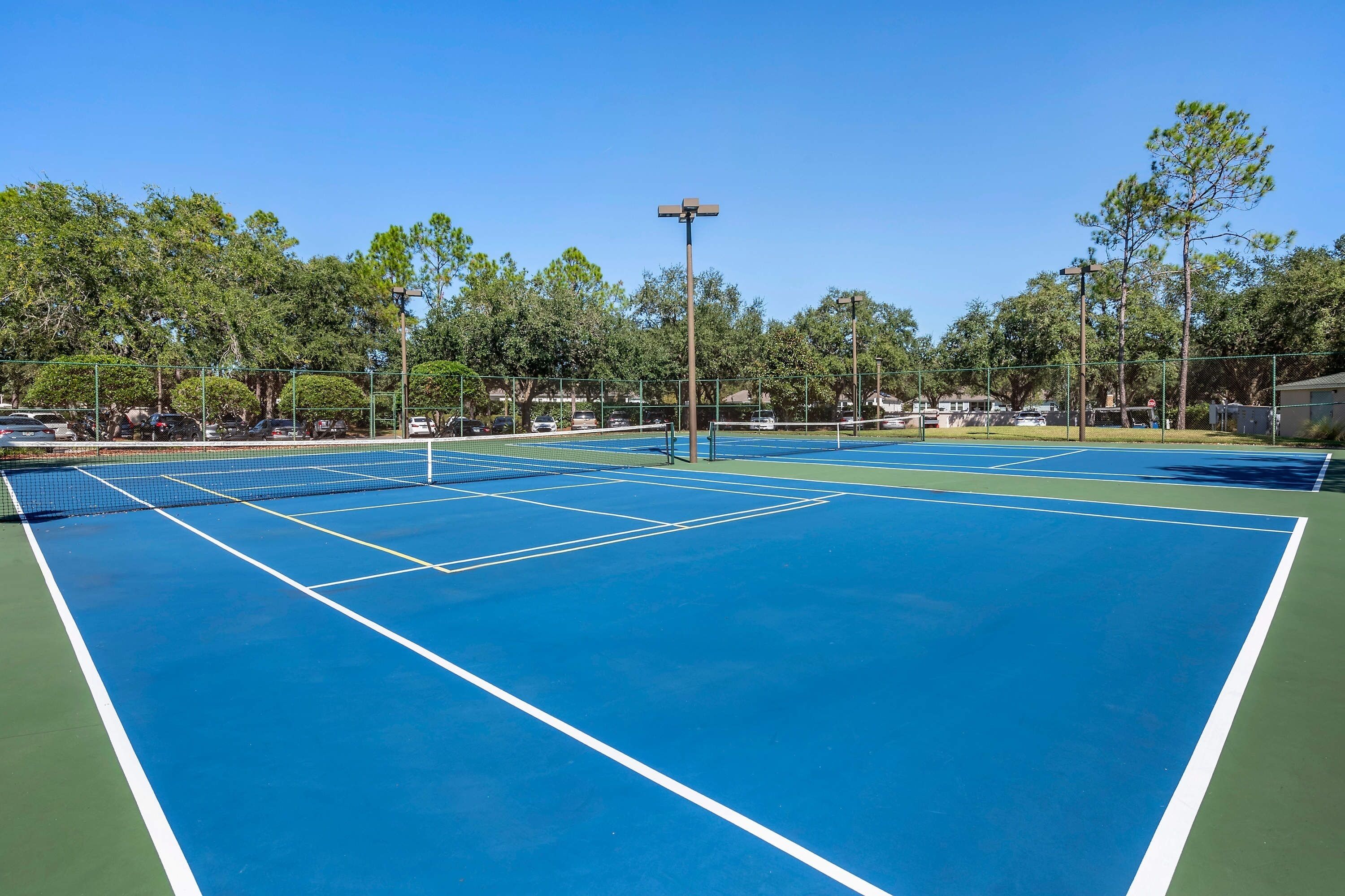 Un court de tennis comprenant plusieurs terrains, entouré d’arbres et d’une clôture.