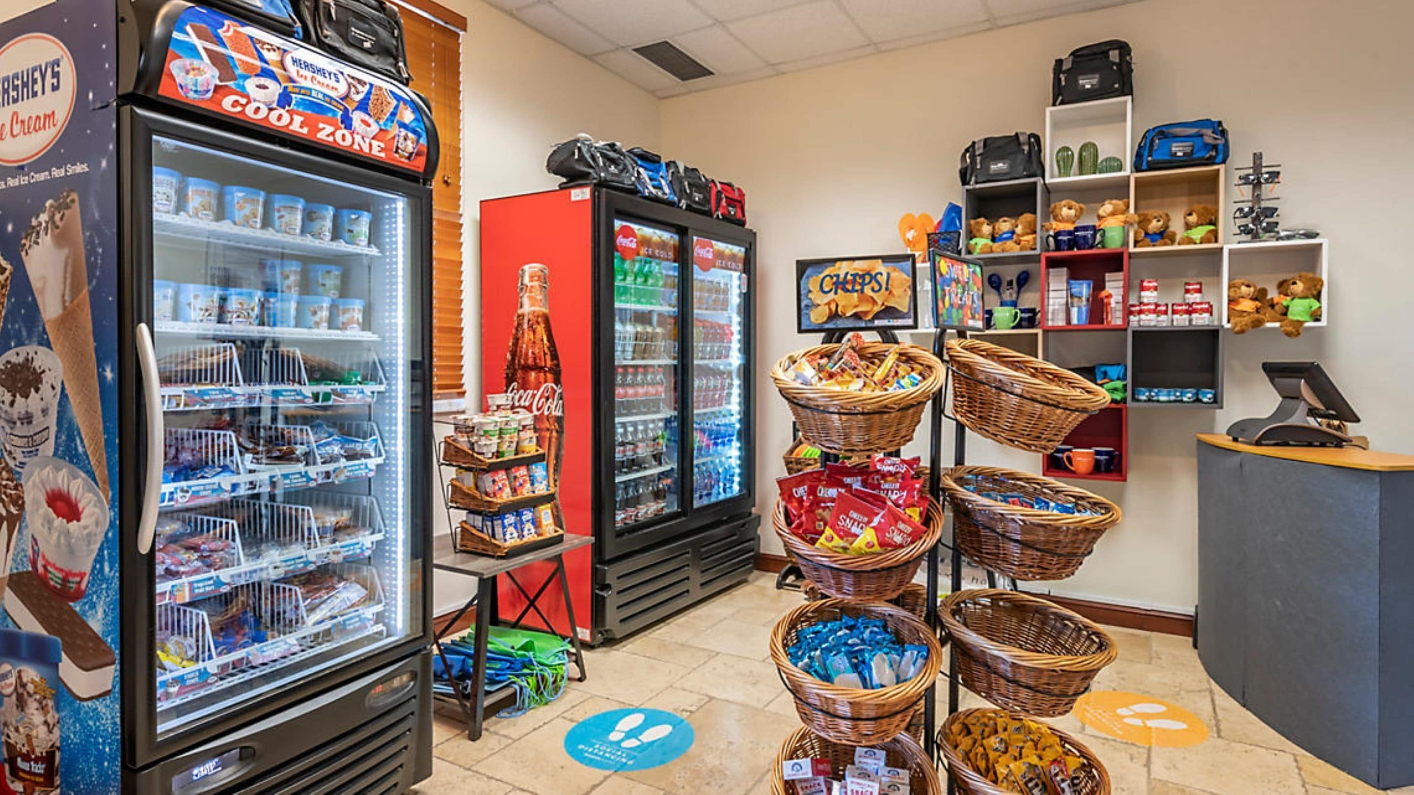 A convenience store with a refrigerated display of snacks, a Coca-Cola cooler, and baskets of snacks.