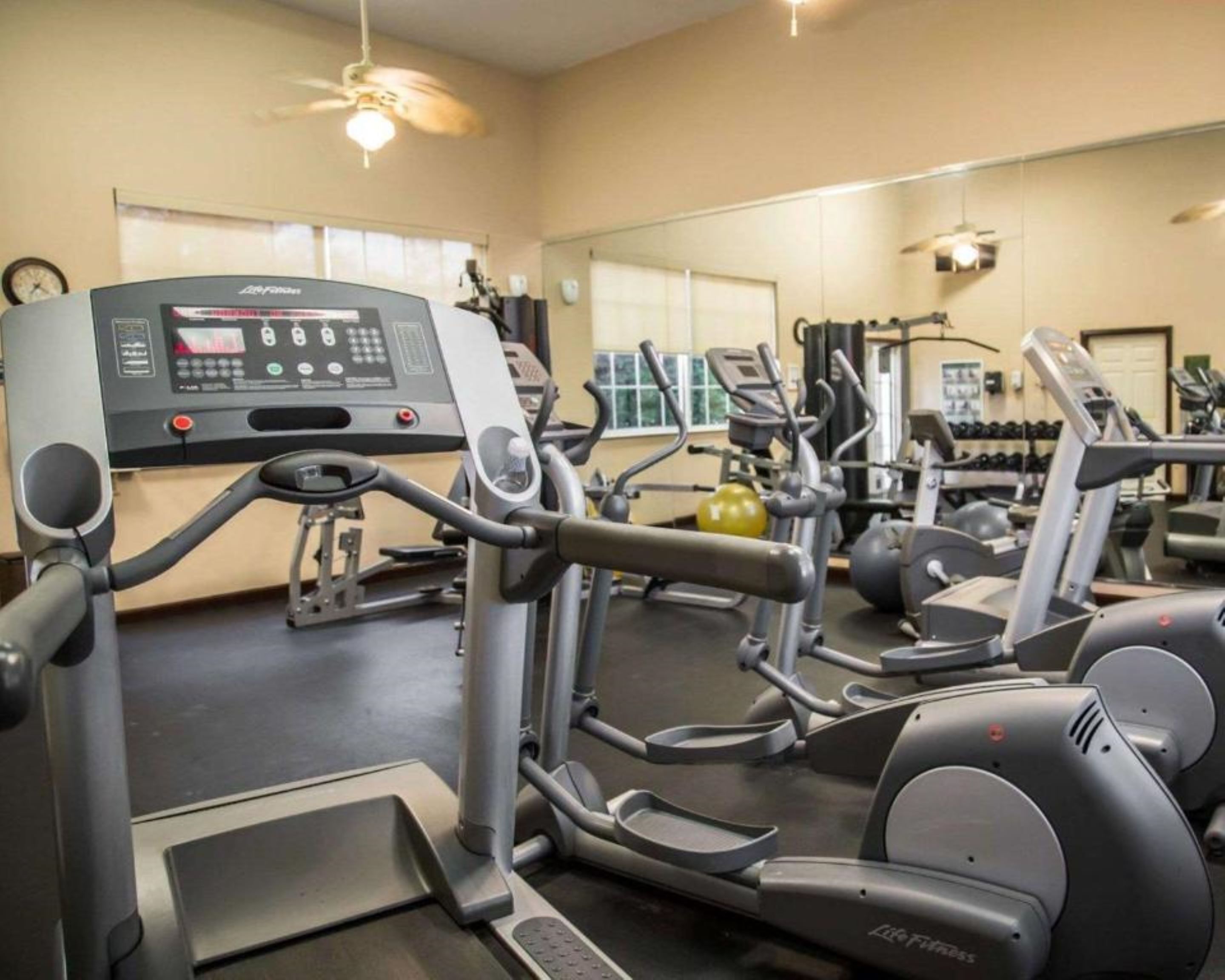 A gym with cardio machines, weight equipment, and a mirrored wall.