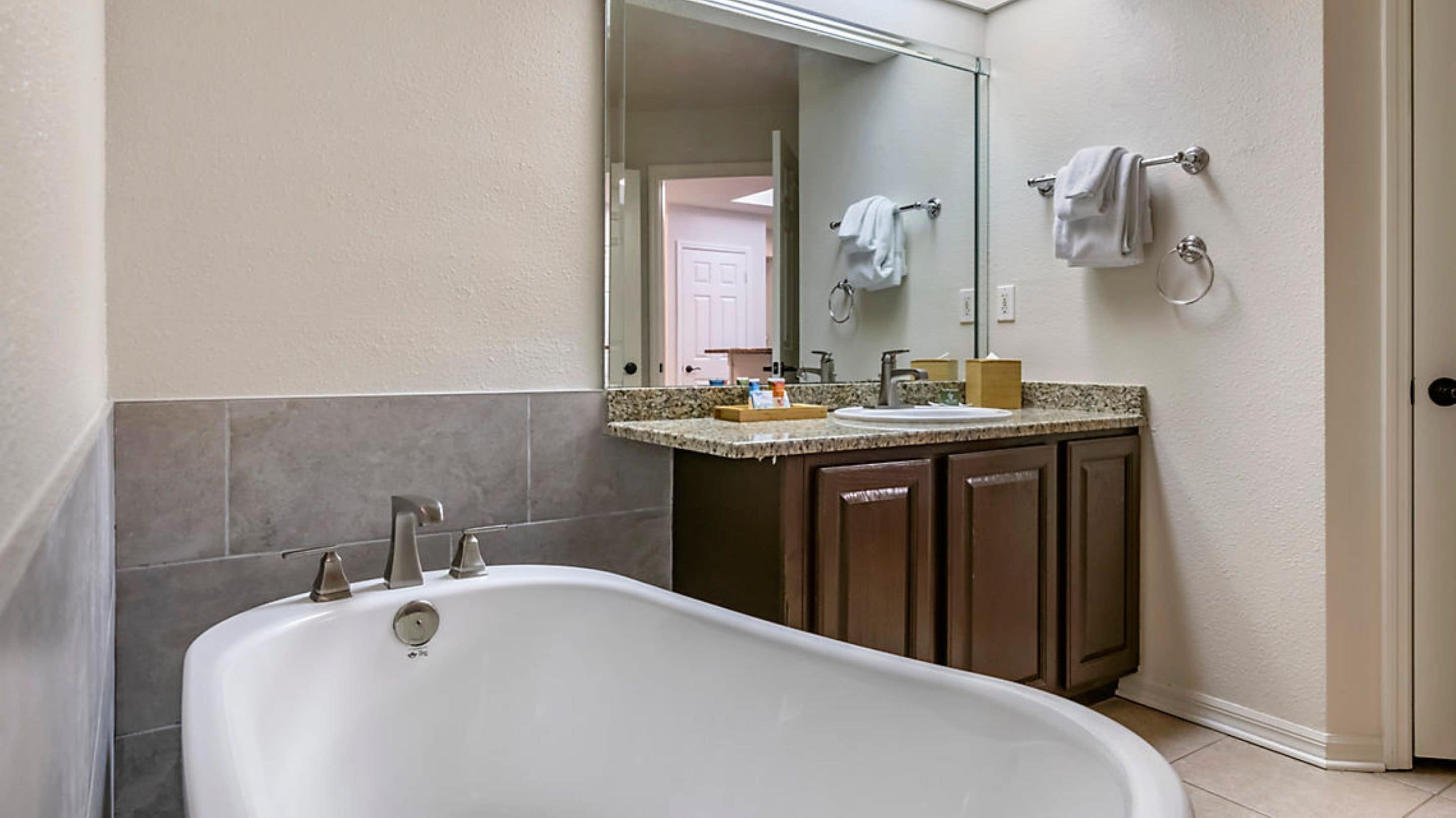 Un bagno con una vasca freestanding, un lavabo e uno specchio sopra. Asciugamani appesi a un portascopevoli e una porta che dà su un'altra stanza sono visibili sullo sfondo.