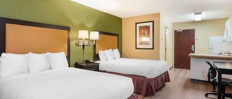 A hotel room with two beds, a desk, a chair, and a small kitchenette.