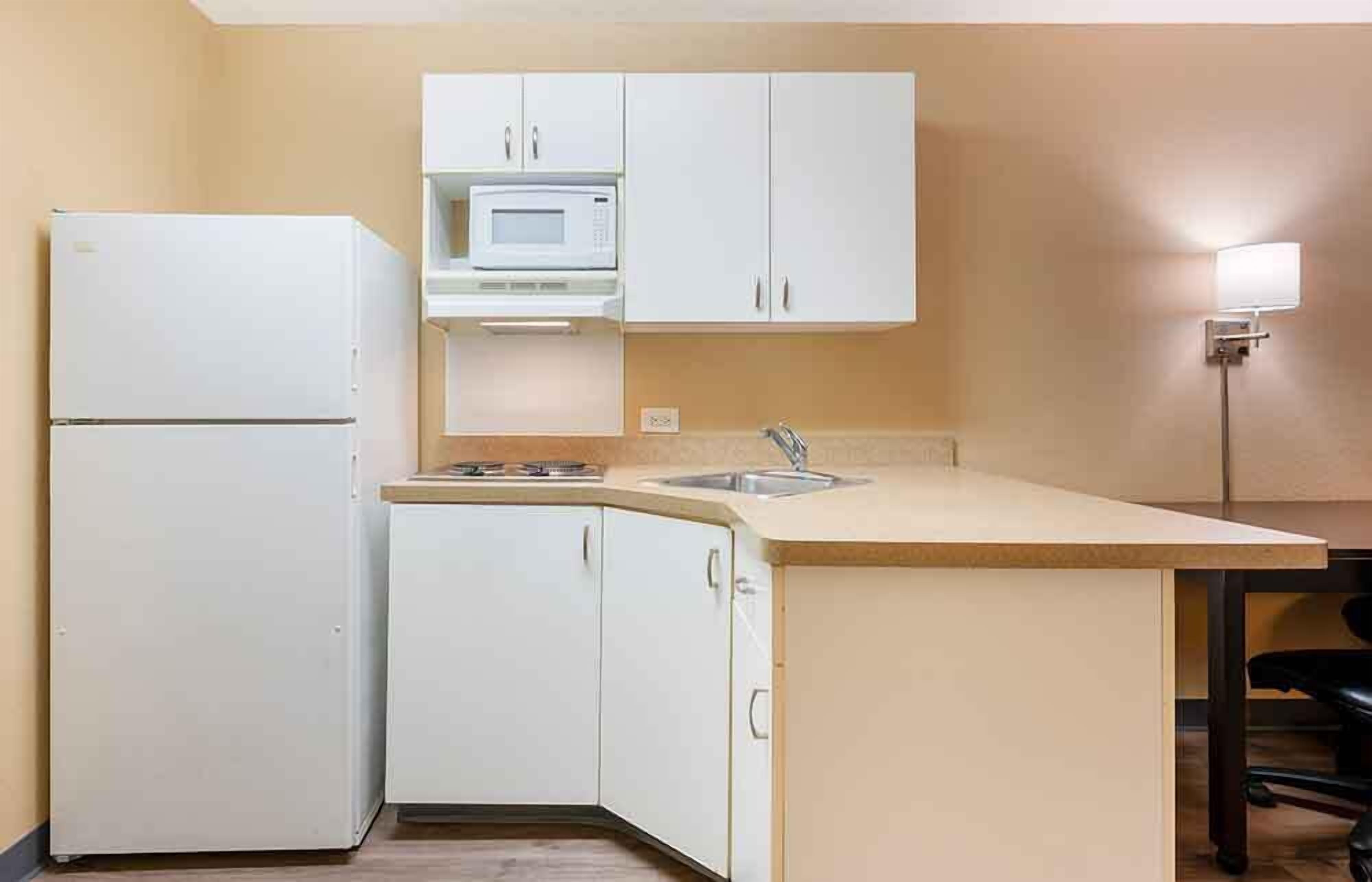 A compact kitchen with white cabinets, a microwave, a sink, and a refrigerator.
