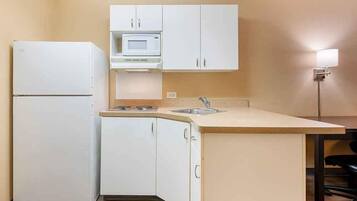 A compact kitchen with white cabinets, a microwave, a sink, and a refrigerator.