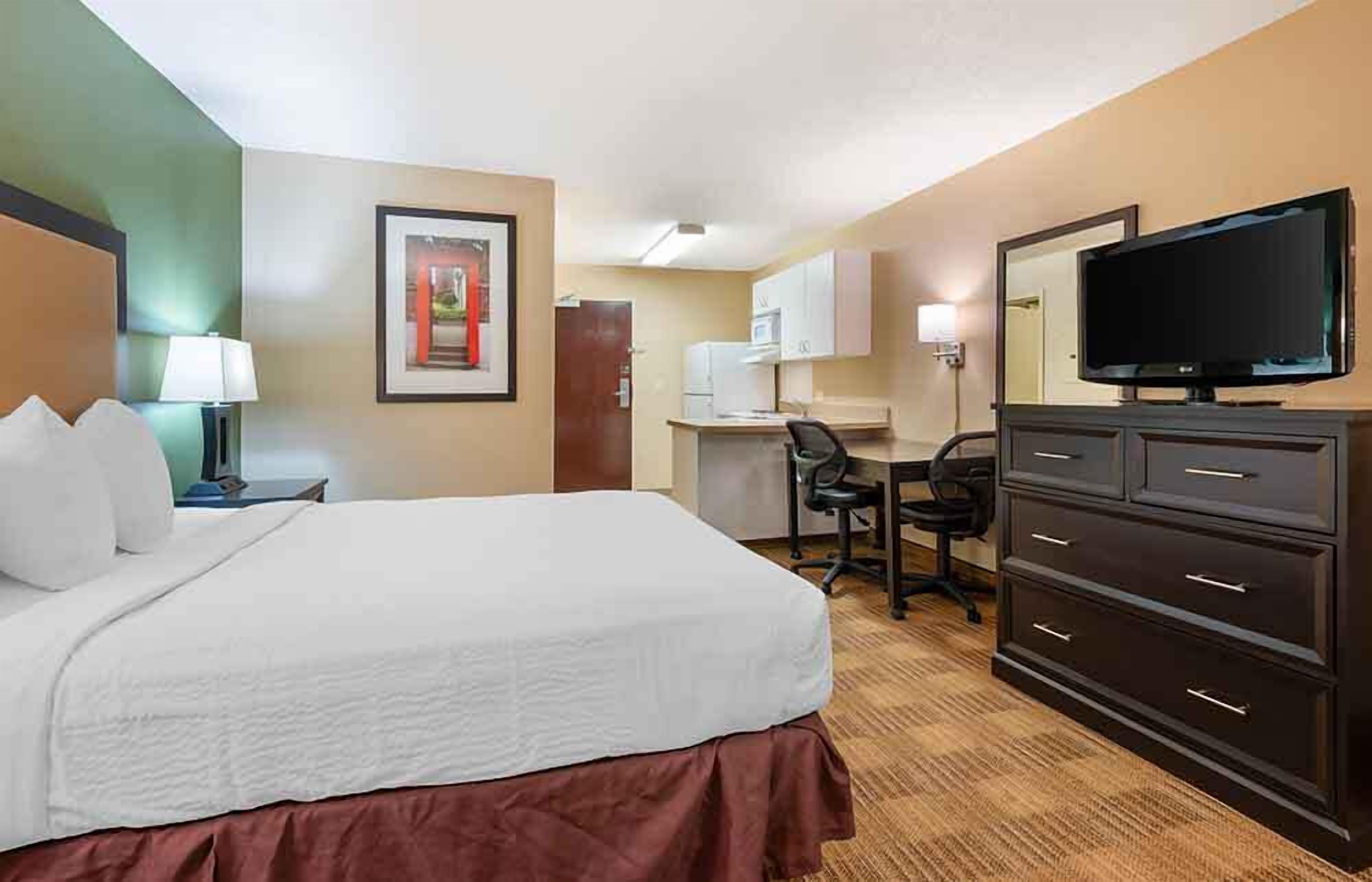 Een hotelkamer met een bed, bureau, stoel, dressoir, televisie en een ingelijst schilderij aan de muur.