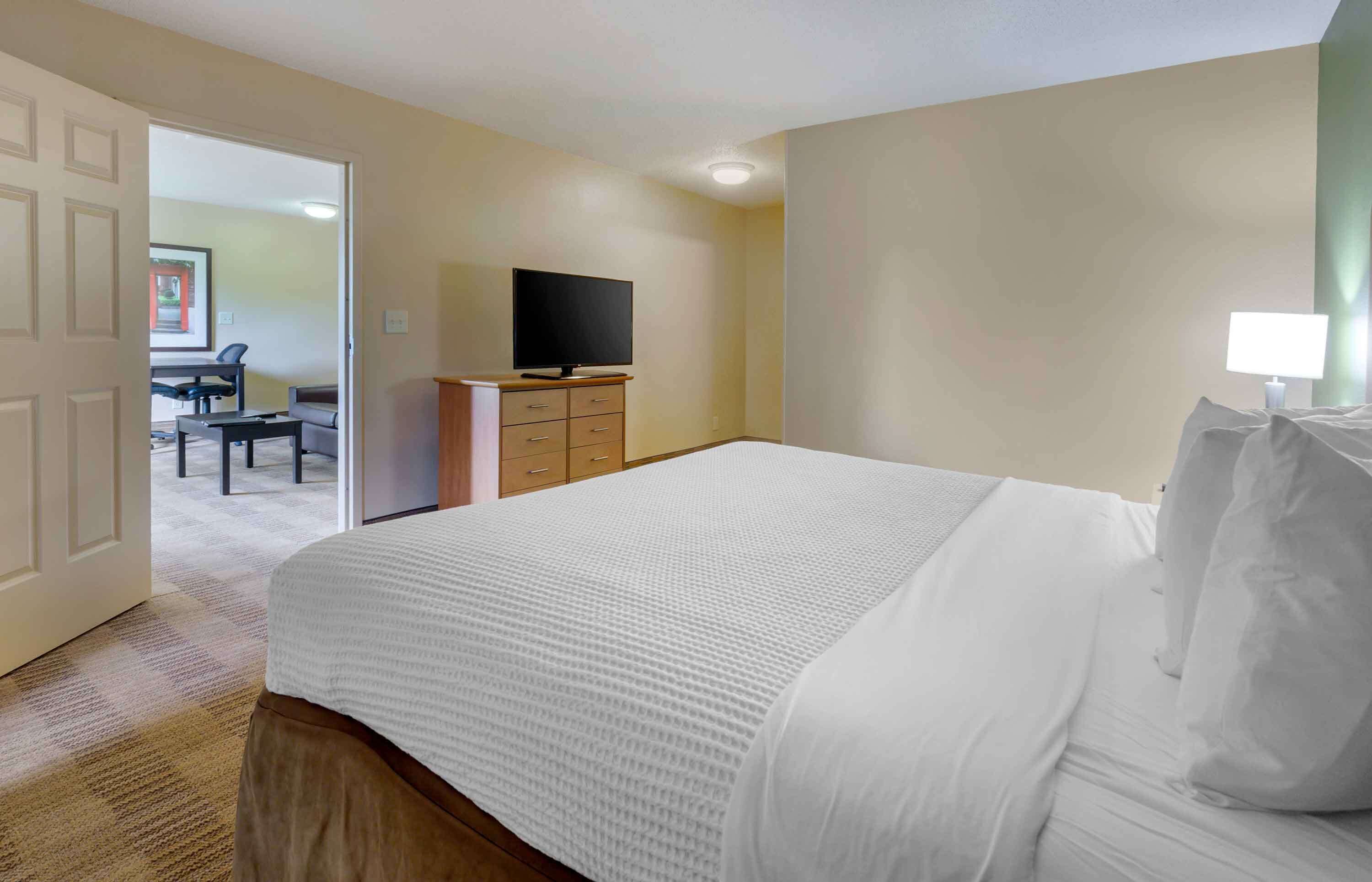 A hotel room with a large bed, a desk with a flat-screen TV, and a chair.