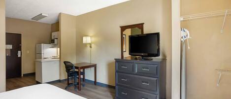A hotel room with a bed, a desk with a chair, a television, a refrigerator, and a microwave.