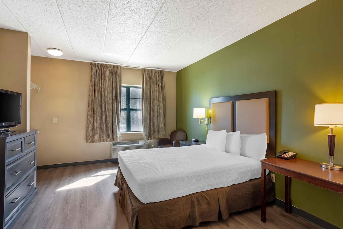 A hotel room with a large bed, a desk, a chair, a television, and a window with curtains.