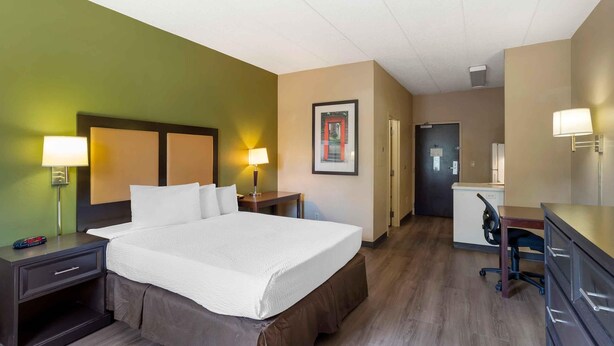 Een hotelkamer met een groot bed, twee nachtkastjes met lampen, een bureau met een stoel, en een deur naar een badkamer.