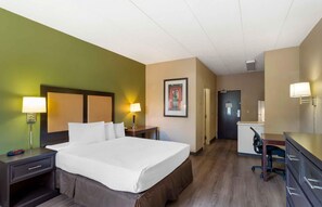 A hotel room with a large bed, two bedside tables with lamps, a desk with a chair, and a door leading to a bathroom.