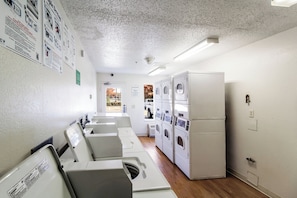 Un cuarto de lavandería con varias lavadoras y secadoras, una puerta que da al exterior e instrucciones de seguridad en las paredes.