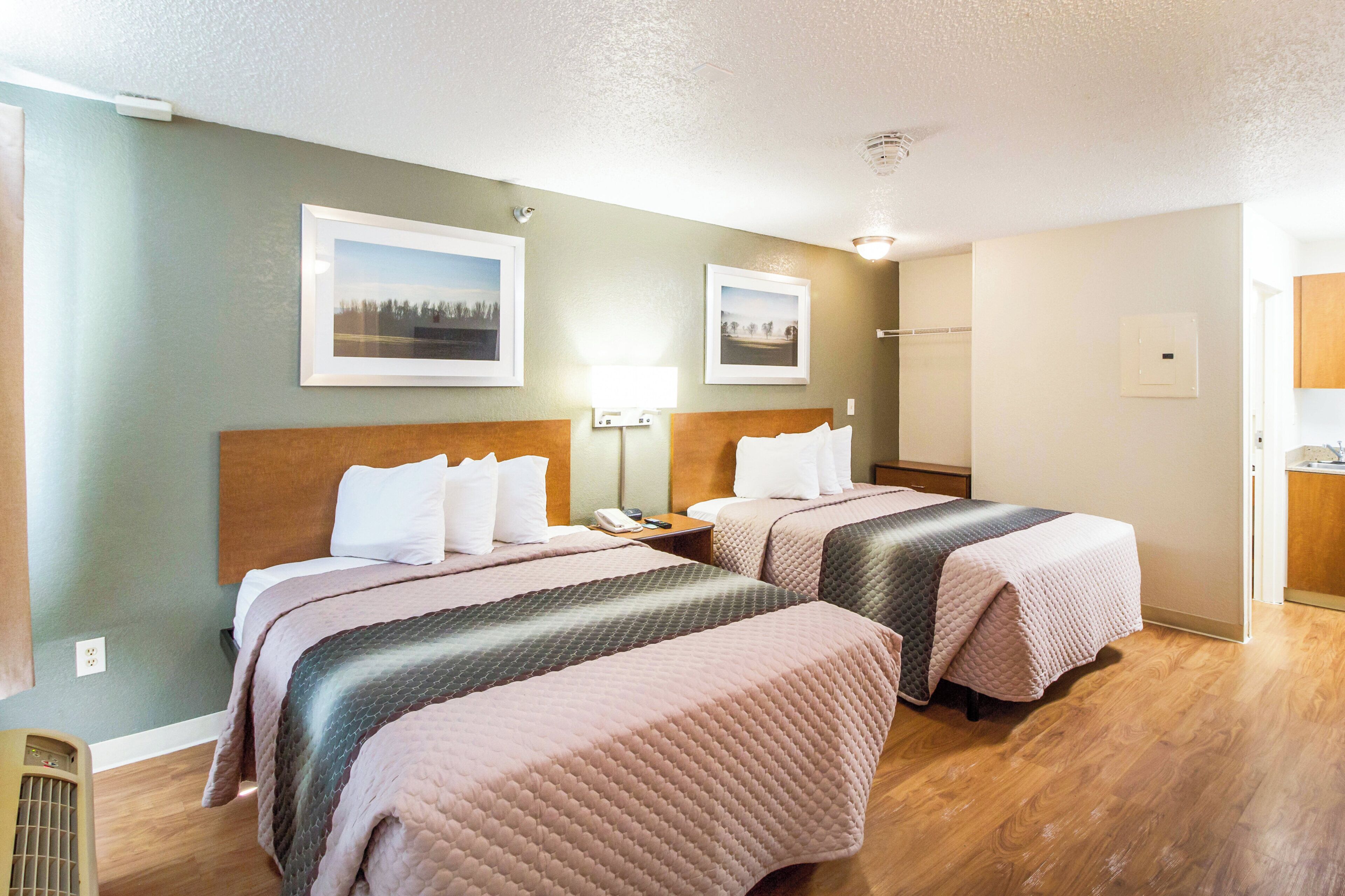 A hotel room with two beds, a wooden headboard, a nightstand, a telephone, and two framed pictures on the wall.