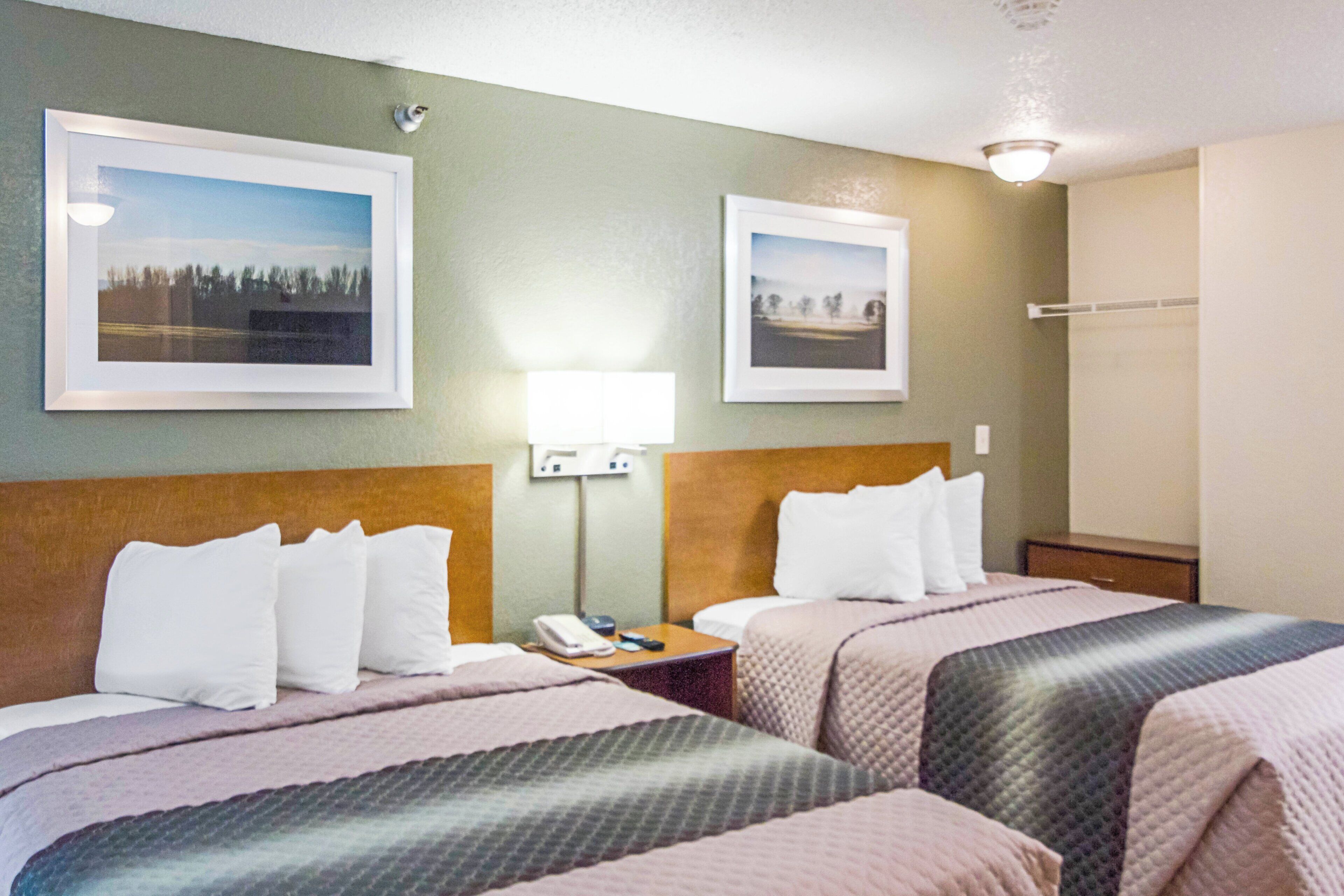 A hotel room with two beds, a nightstand with a phone, a lamp, and two framed pictures on the wall.