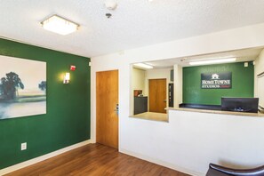 A reception area with a green wall, a wooden door, and a reception desk with a sign for 'HOMETOWN STUDIOS by Red Roof'. - HomeTowne Studios by Red Roof Houston - West Oaks/ Energy Corridor (Houston)