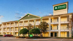Un hotel de varios pisos con un letrero de entrada verde, balcones y estacionamiento.