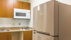 A kitchen with wooden cabinets, a white microwave, and a white refrigerator. - HomeTowne Studios by Red Roof Houston - West Oaks/ Energy Corridor (Houston)