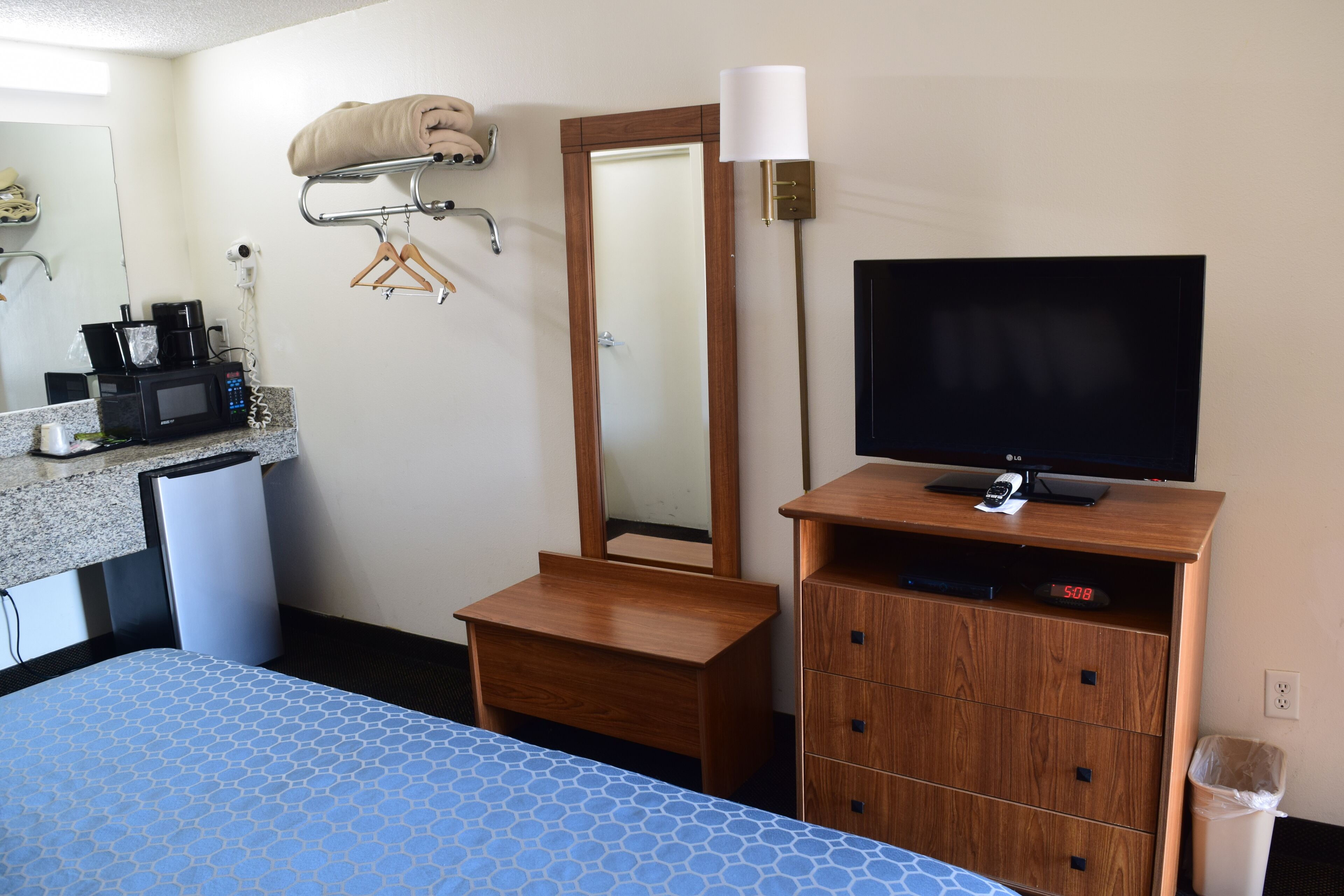 Camera d'albergo con un letto, una cassettiera in legno con una TV, uno specchio, un forno a microonde e una piccola scrivania con una macchina da caffè.