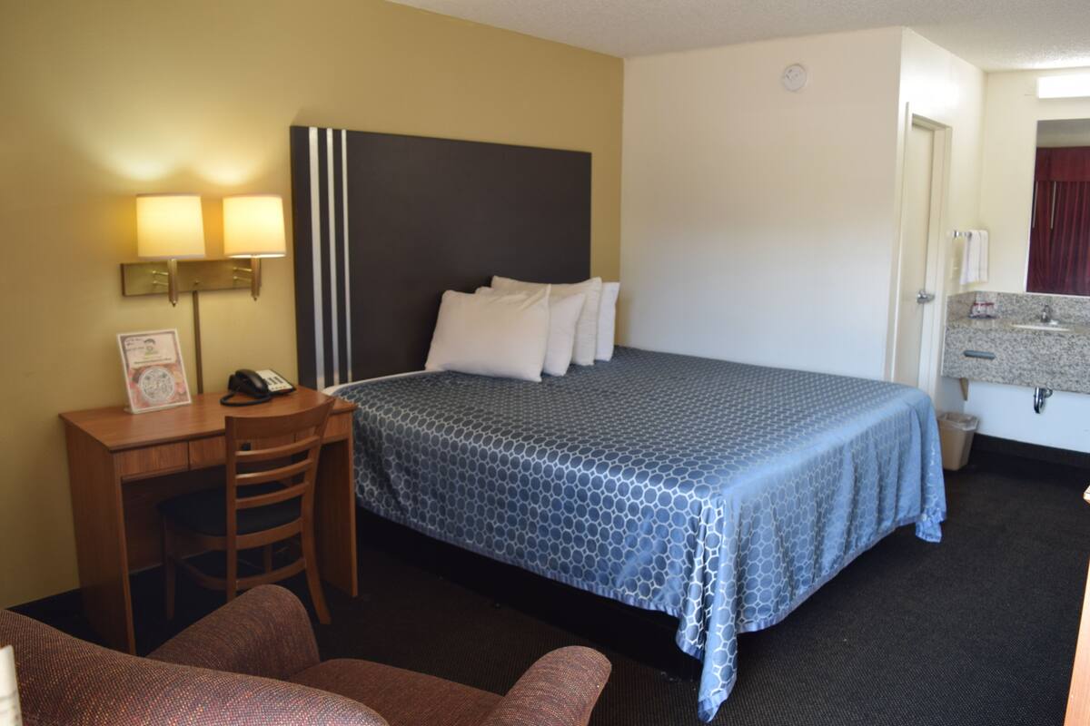 A hotel room with a bed, a desk with a chair, a lamp, and a small table with a telephone.