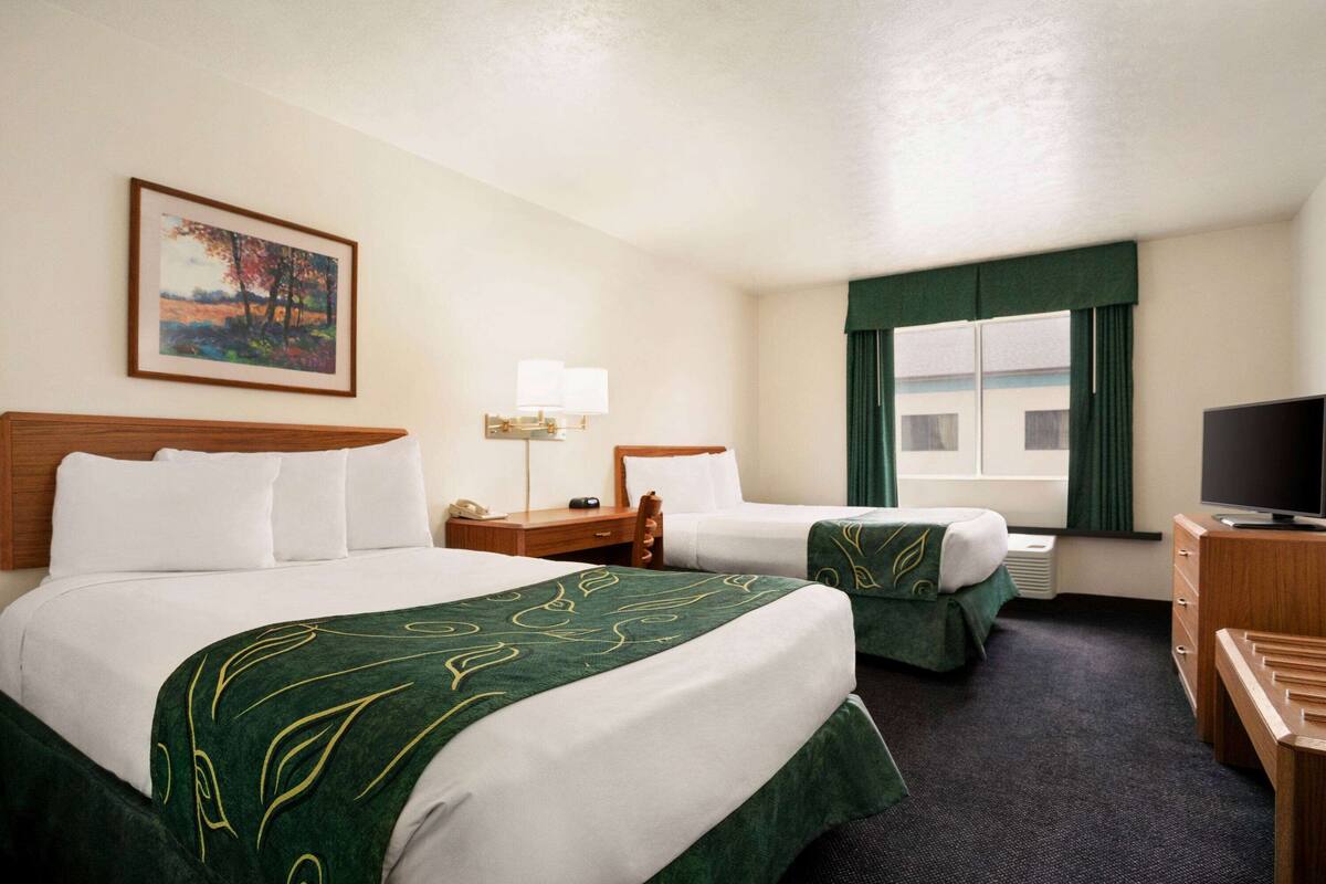 A hotel room with two beds, a desk, a television, and a painting on the wall.