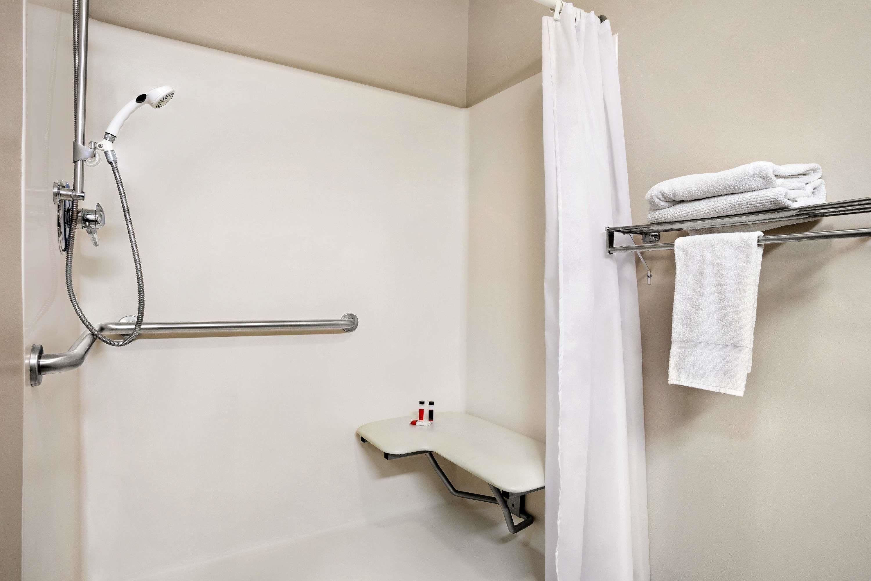 A shower with a handheld showerhead, a towel rack with folded towels, and a small shelf with a bottle.