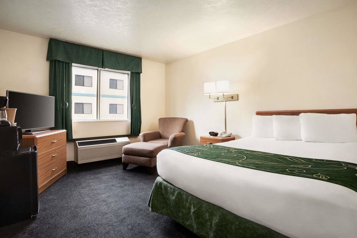 A hotel room with a bed, a chair, a desk with a television, and a window with curtains.