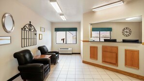 Un área de recepción con mostrador, un reloj, una ventana y una zona de estar con dos sillones y una mesa.