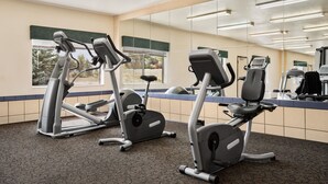 Un gimnasio con bicicletas estáticas, cinta de correr y un espejo grande.