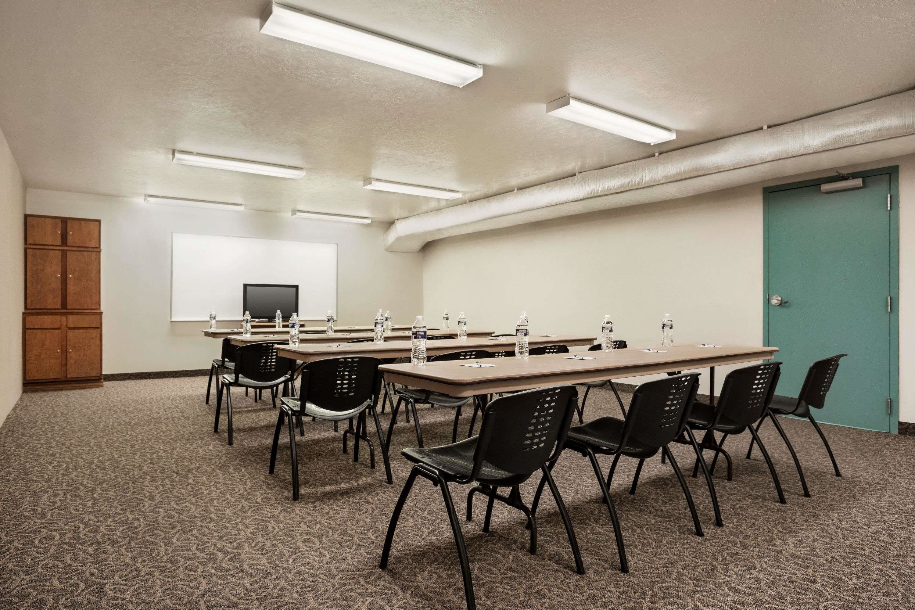 A conference room with a long table, black chairs, a projector screen, and a teal door.