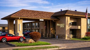Un motel appelé « Discovery Inn », doté d’une entrée abritée, avec une voiture rouge garée devant et un drapeau américain.