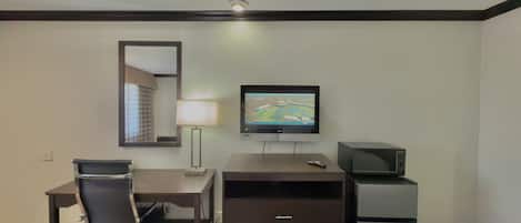 Habitación de hotel con escritorio, silla, televisor, lámpara y refrigerador pequeño.
