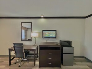 A hotel room with a desk, chair, TV, lamp, and a small refrigerator. - Discovery Inn (Midvale)