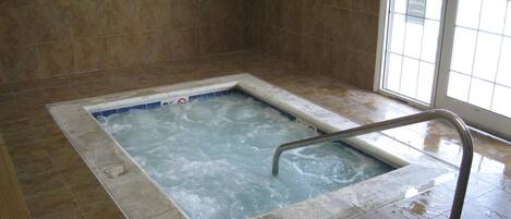 Un jacuzzi con una escalera metálica, rodeado de paredes y suelo de baldosas.