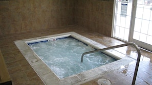 A hot tub with a metal ladder, surrounded by tiled walls and floor.