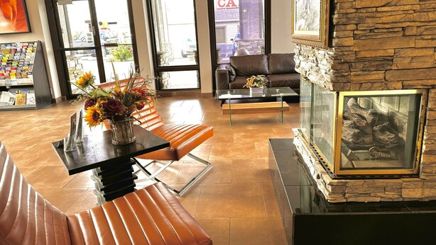 A modern lobby with leather seating, a glass coffee table, a stone fireplace, and a view of the outside through large windows. - Discovery Inn (Midvale)