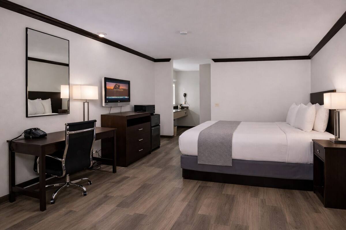 A hotel room with a bed, desk, chair, TV, and a mirror.